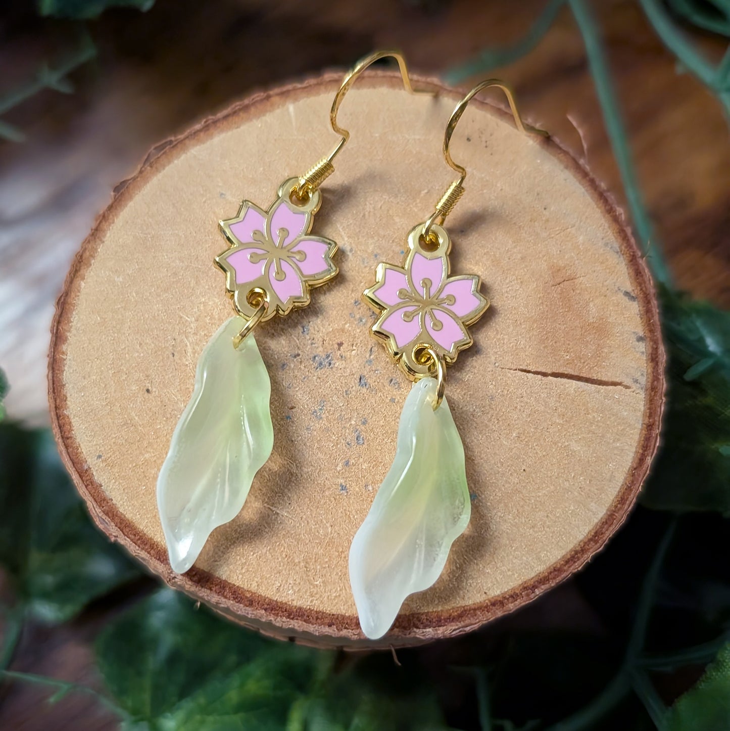 Pair of hook earrings with pink floral charms and green leaf-like pendants on a wooden surface.