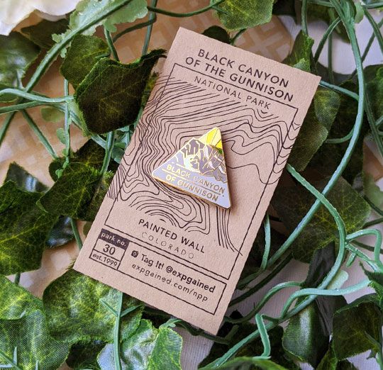 Triangle Black Canyon of the Gunnison national park enamel pin featuring a view from the beehive hike on a brown business card size backing card with a topo map of the Painted Wall.