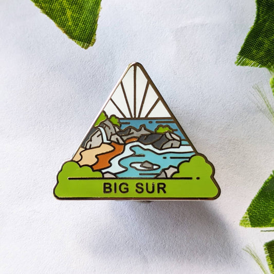 A hard enamel pin with a design representing the Big Sur region of California, featuring a stylized coastline and mountains.