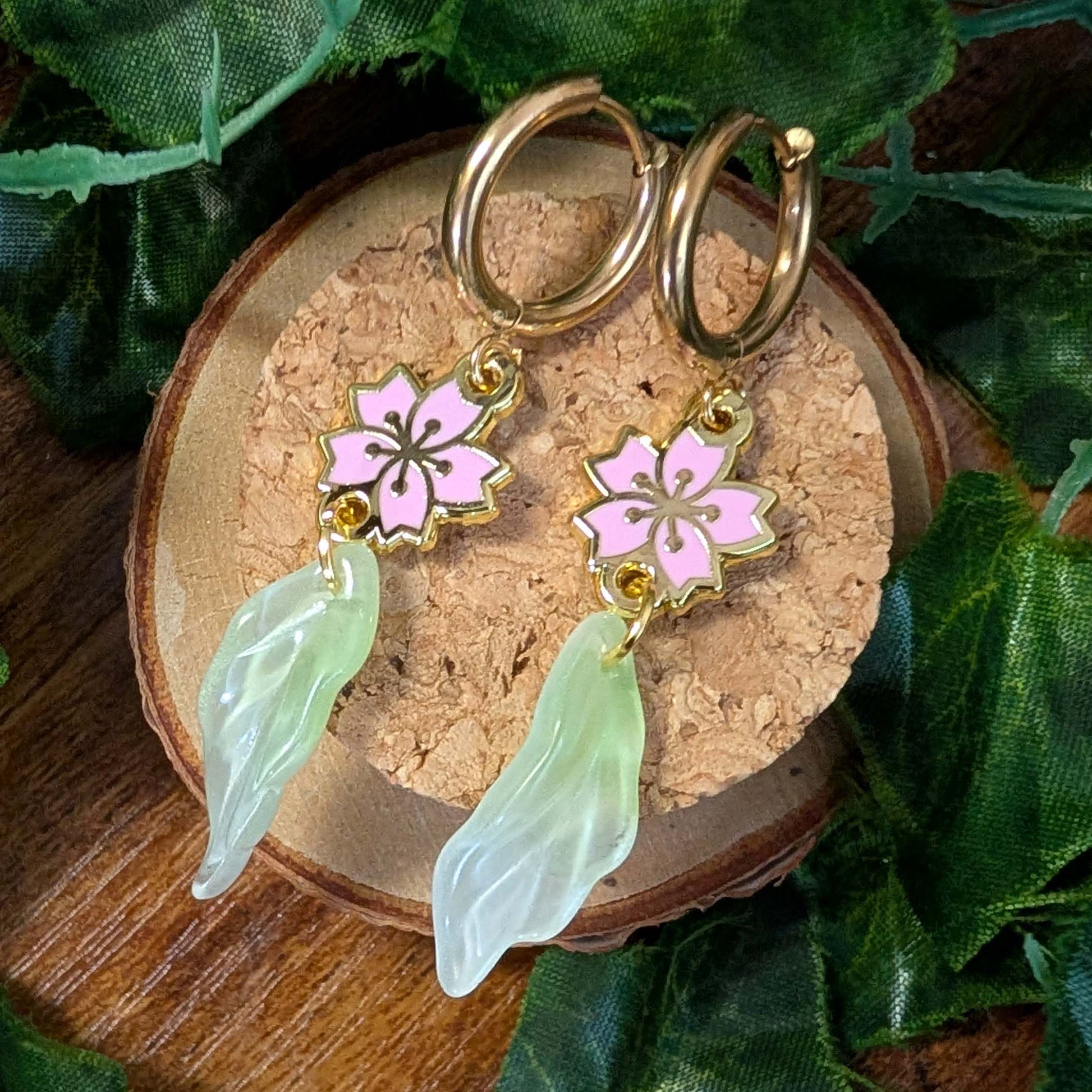 Pair of hoop earrings with pink floral charms and green leaf-like pendants on a wooden surface.