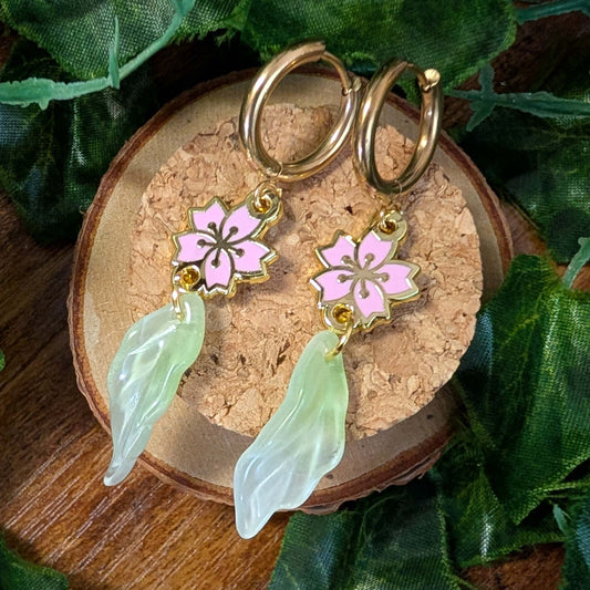 Pair of hoop earrings with pink floral charms and green leaf-like pendants on a wooden surface.