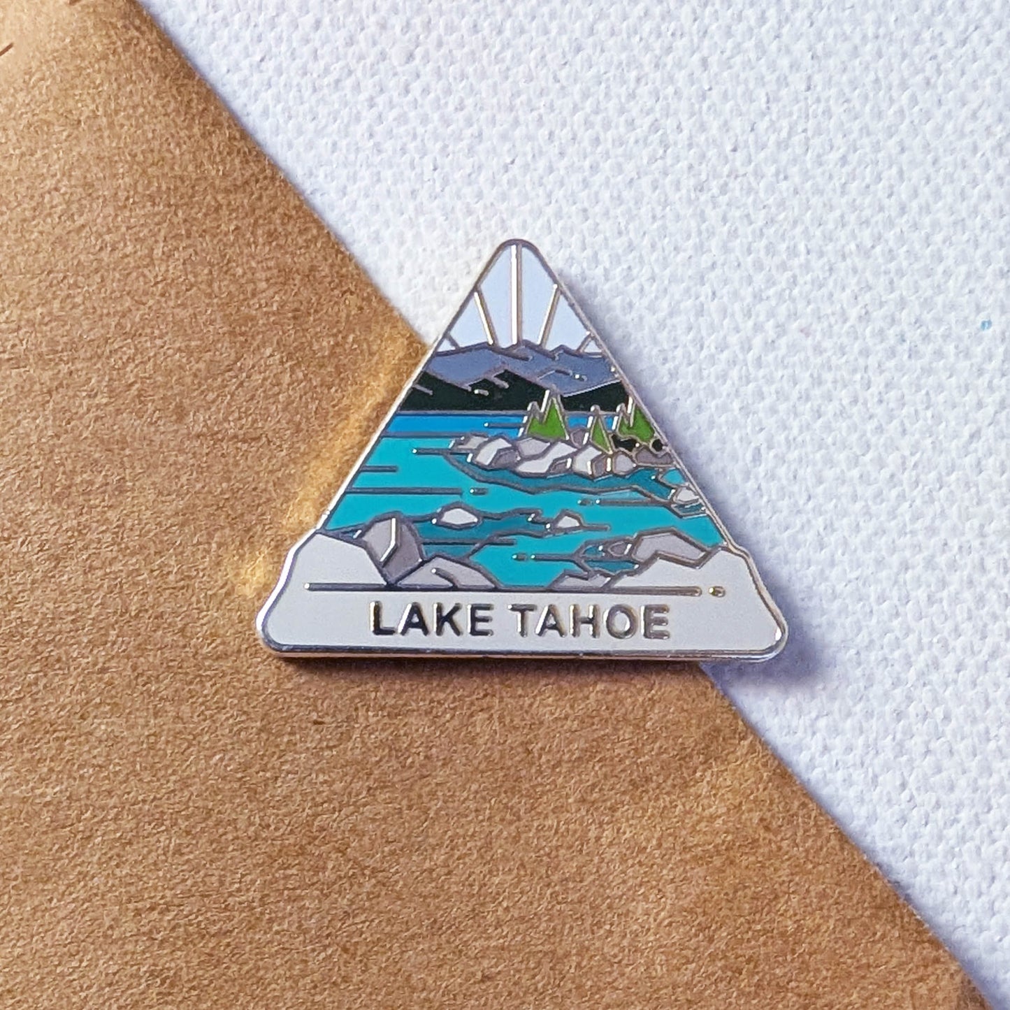Triangular enamel pin of Lake Tahoe on a textured surface