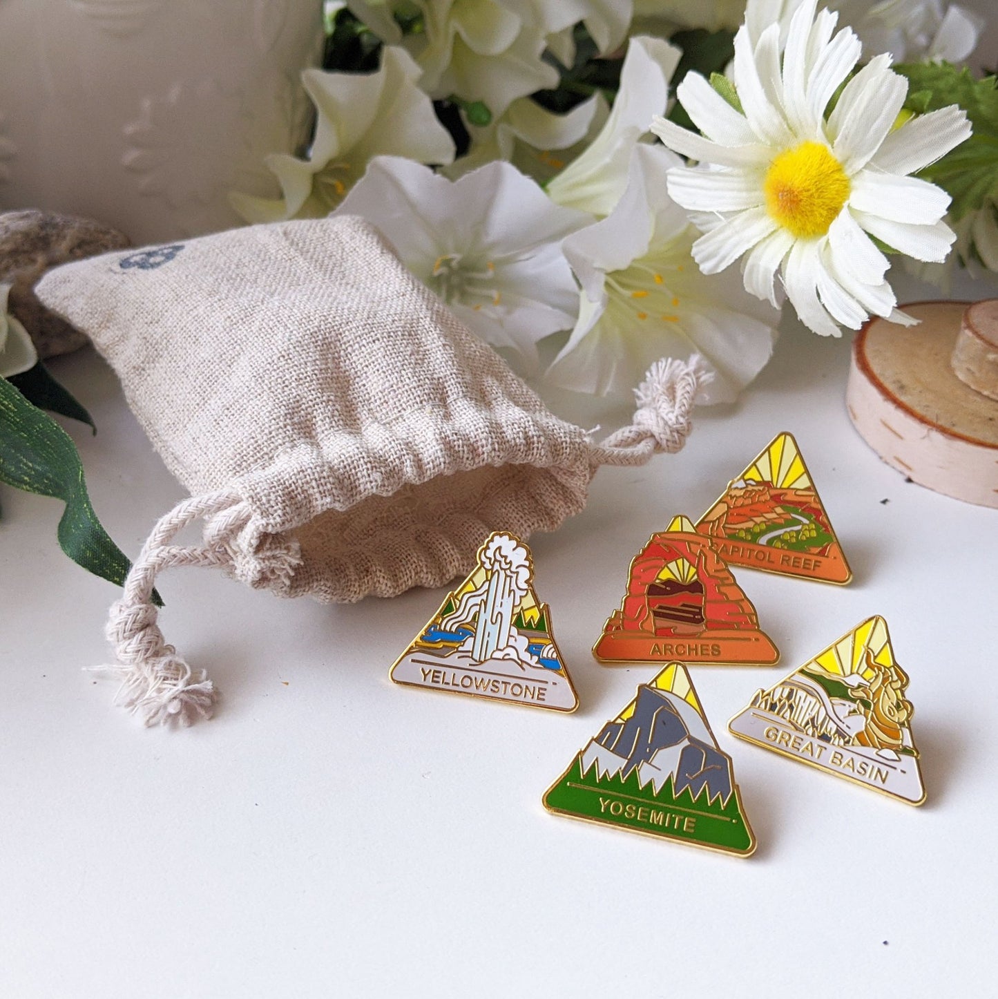 Small muslin bag with national park pins featuring designs including yellowstone, arches, capitol reef, yosemite, and great basin. 