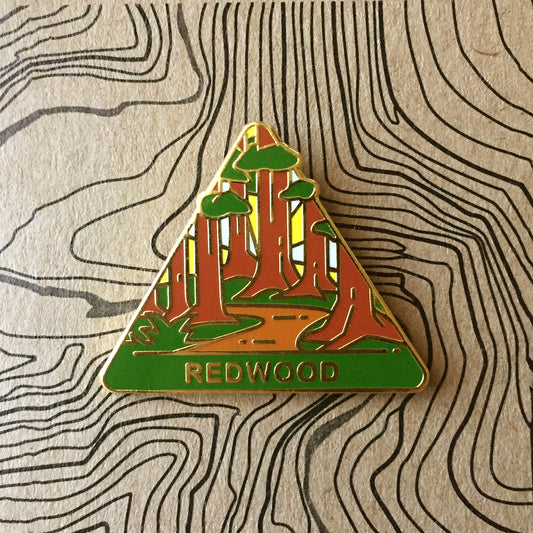 Triangle Redwood national park enamel pin featuring a view of a trail wandering through beautiful redwood trees.