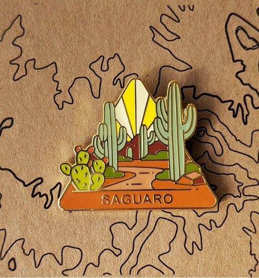 Triangle Saguaro national park enamel pin featuring a view of a trail wandering past tall saguaro cacti.