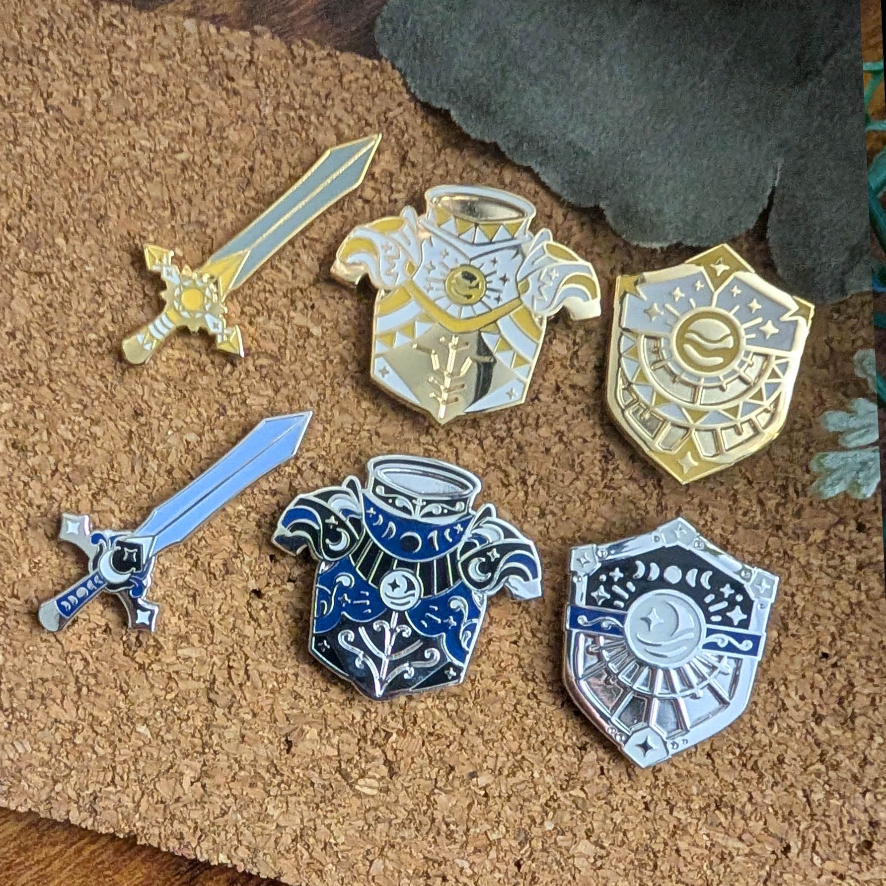 Set of enamel pins including swords and armor on a cork background