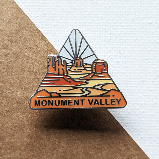 Triangle Monument Valley enamel pin featuring a view of West Mitten Butte, East Mitten Butte, and Merrick Butte..