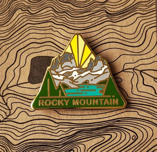 Triangle Rocky Mountain national park enamel pin featuring a view of green turquoise colored Emerald Lake surrounded by peaks and forest.