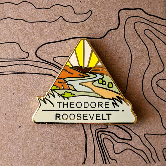 Triangle Theodore Roosevelt national park enamel pin featuring a view of the Little Missouri River flowing through grasslands.